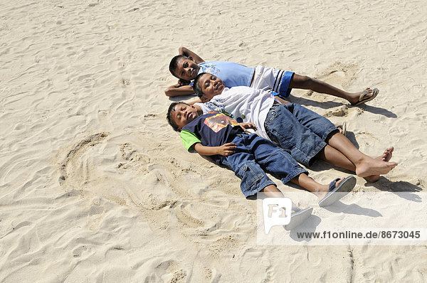 Drei Jungen der Kuna-Indianer liegen im Sand  Nalunega  San Blas Archipel  Panama