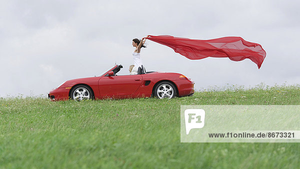 Frau in einem Cabrio lässt ein rotes Tuch im Fahrtwind flattern  Deutschland