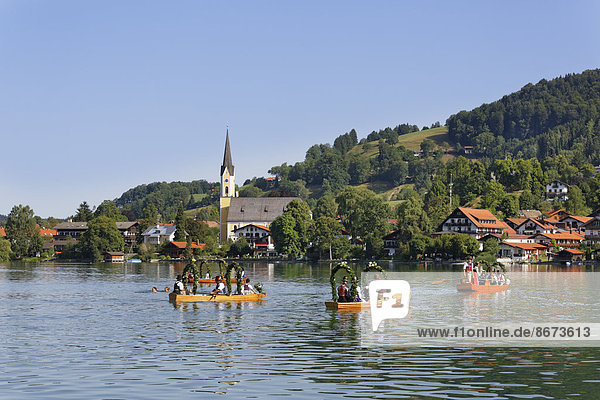 Trachtler in festlich geschmückten Plätten  Holzbooten  hinten die Kirche St. Sixtus  Alt-Schlierseer-Kirchtag  Schliersee  Oberbayern  Bayern  Deutschland