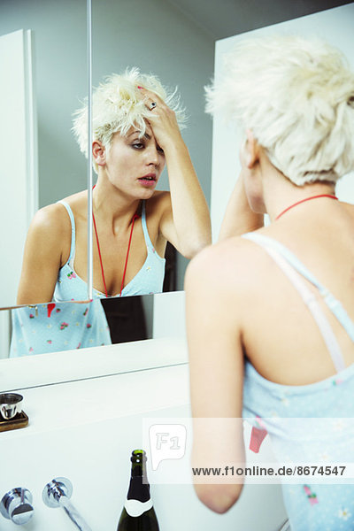 Hungover woman examining herself in mirror