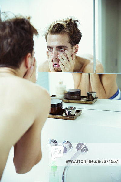 Hungover man examining himself in mirror