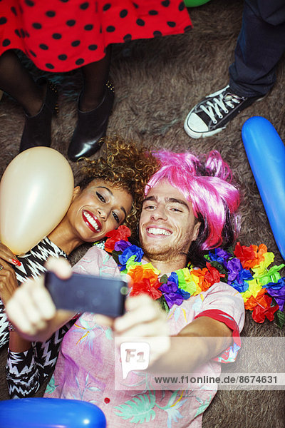 Couple taking self-portraits with camera phone on floor at party