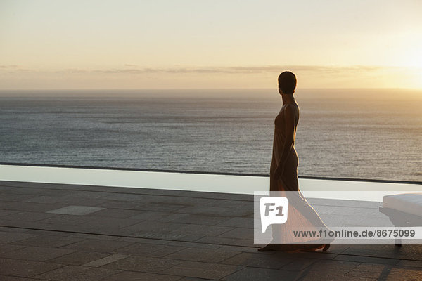 Frau blickt von der modernen Terrasse bei Sonnenuntergang auf den Ozean