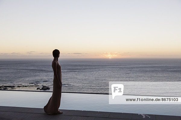 Frau schaut von der Terrasse auf den Ozean