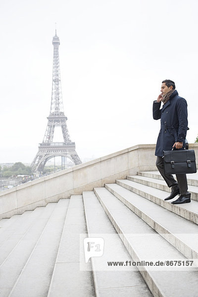 Businessman talking on cell phone on steps near Eiffel Tower  Paris  France