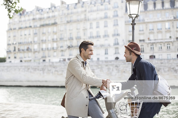 Businessmen handshaking on bicycles along Seine River  Paris  France