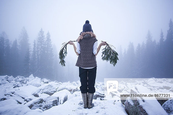 Caucasian woman holding tree branches on snow covered rocks