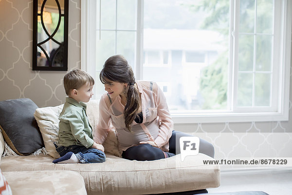 Pregnant Caucasian mother sitting with son in living room