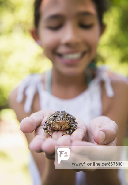 Mixed race girl holding frog outdoors