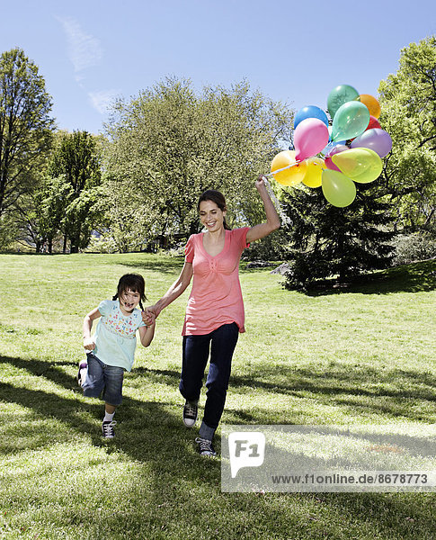 Mixed race mother and daughter holding balloons in park