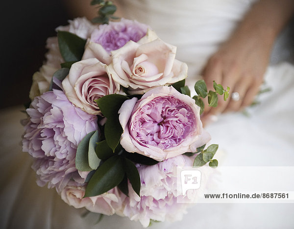 Eine Frau  eine Braut  die einen Brautstrauß aus pastellfarbenen zartrosa Rosen und Pfingstrosen hält.