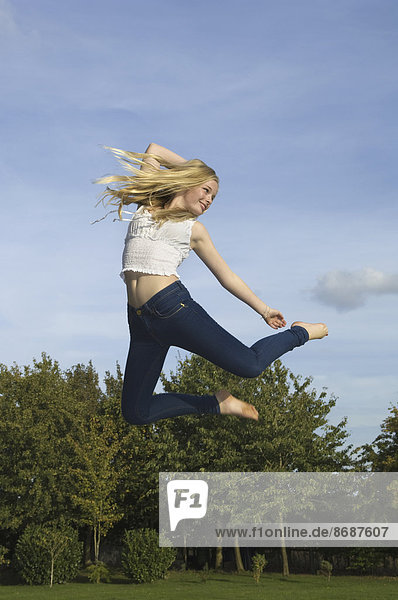 Teenager-Mädchen mit langen blonden Haaren springt in die Luft.
