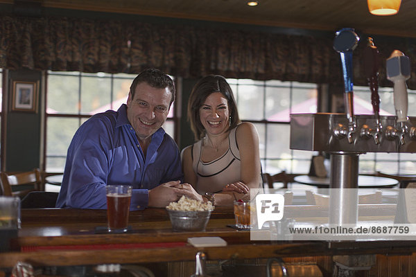 Ein Mann und eine Frau sitzen lächelnd nebeneinander an einer Bar. Bei einer Verabredung.