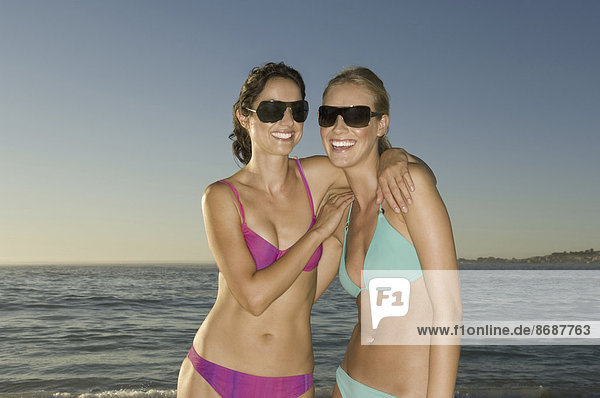 Zwei junge Frauen am Strand von Kapstadt  in Bikinis und mit Sonnenbrille.