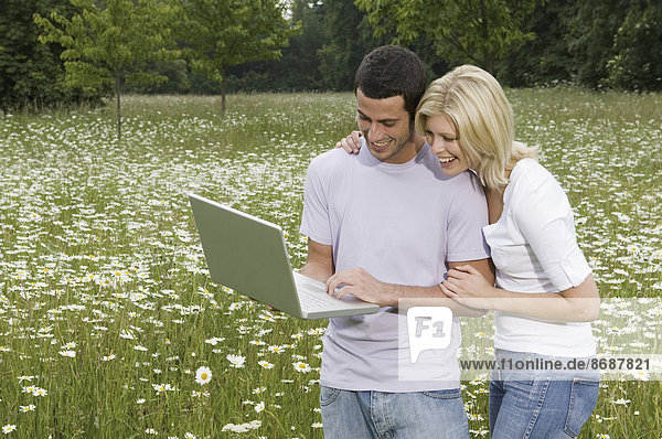 Ein Mann und eine Frau auf einer Blumenwiese  die auf einen Laptop-Bildschirm schauen.