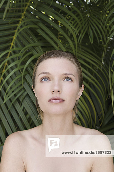 Eine junge Frau mit nackten Schultern  die nach oben schaut. Tropische Pflanzen im Hintergrund.