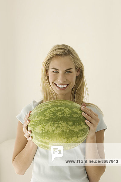 Eine Frau hält eine große grüne Wassermelone in der Hand.
