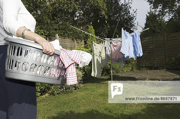 Eine Frau  die einen Wäschekorb zur Wäscheleine trägt.