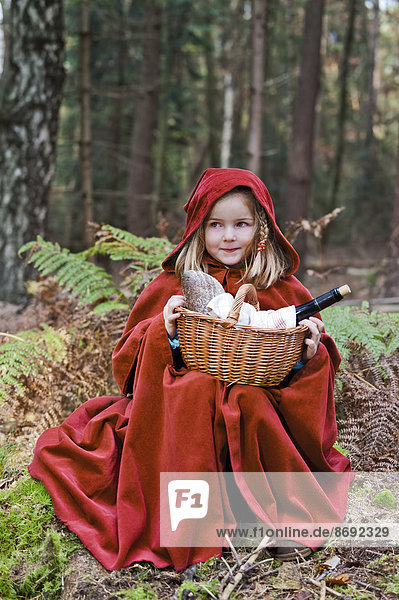 Kleines Mädchen verkleidet als Rotkäppchen im Wald sitzend