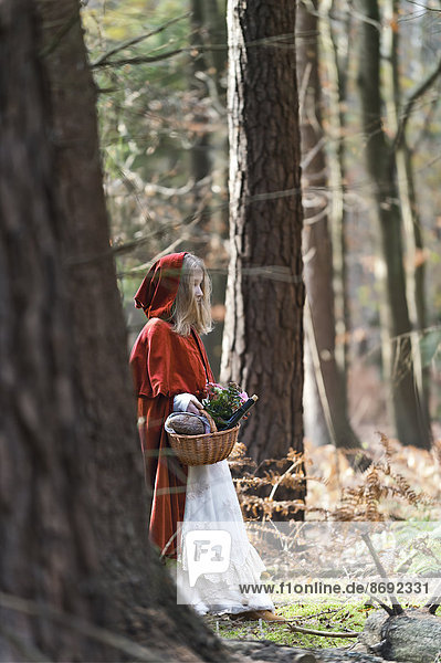 Girl masquerade as Red Riding Hood standing in the wood