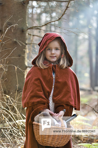 Porträt des kleinen Mädchens als Rotkäppchen im Wald stehend