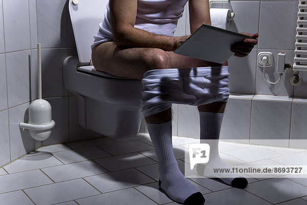 Germany  Man sitting on toilet  using digital tablet