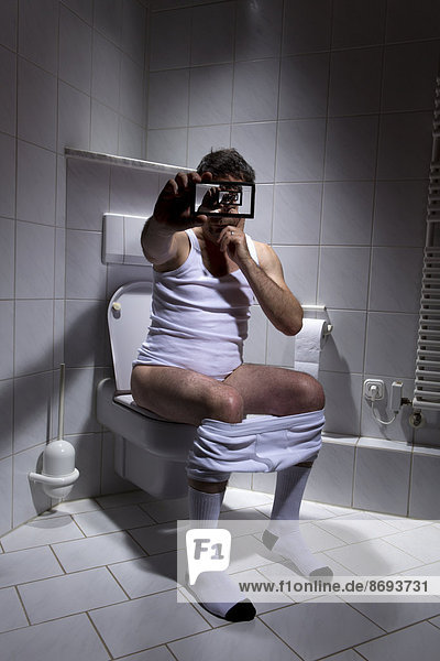 Germany  Man sitting on toilet  using smart phone