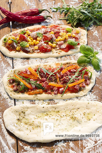 Roher Pizzateig  mit Schinken  Käse  Tomaten  Rucola  Mais  Paprika  Knoblauchöl und Basilikum