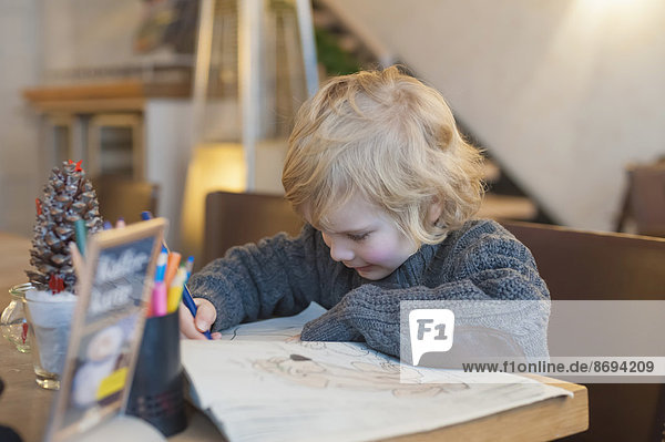 Blond boy in a cafe drawing