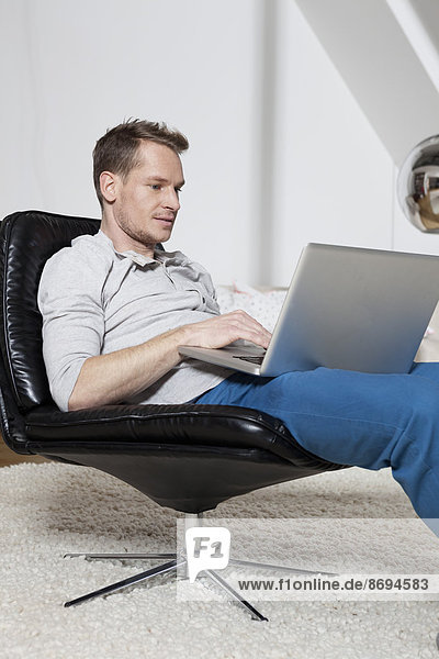 Mann zu Hause entspannt im Sessel mit Laptop