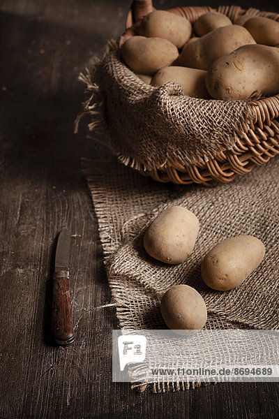 Korb mit Kartoffeln  Messer und Jute auf Holztisch