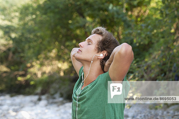 Österreich  Salzkammergut  Mondsee  junger Mann mit Kopfhörer zum Entspannen am Bach