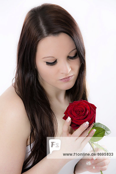 Junge Frau blickt nachdenklich auf rote Rose