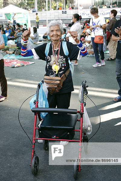 Old woman with a wheeled walker dancing amongst the protesters  political protest  anti government protest  anti-corruption protest at Lumpini Park  Bangkok  Thailand