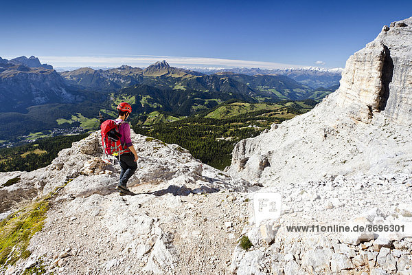 Mountain climber descending from Heiligkreuzkofel Mountain along the Heiligkreuzkofelsteig climbing route in the Fanes Group in Fanes-Sennes-Prags Nature Park  overlooking the Val Badia valley towards the Puez Group and Peitlerkofel Mountain  Dolomites  Alto Adige  Italy