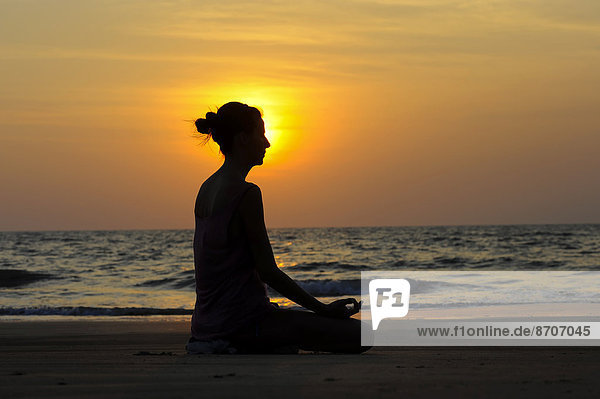 Frau meditiert bei Sonnenuntergang am Strand  Kerala  Indien