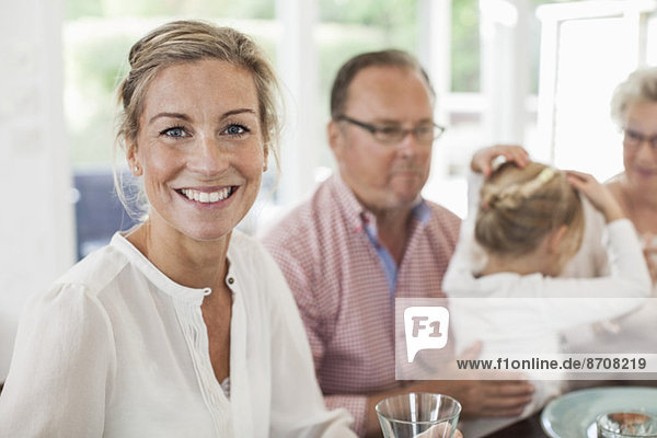 Porträt einer lächelnden Frau am Esstisch mit Familie