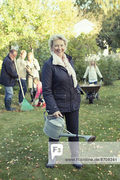 Porträt einer älteren Frau mit Gießkanne bei der Gartenarbeit mit der Familie auf dem Hof.