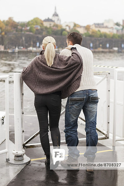 Rückansicht eines jungen Paares  das sich auf ein Geländer im Freien stützt.