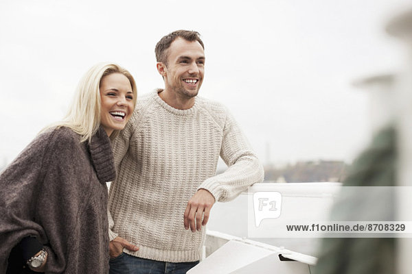 Ein glückliches junges Paar  das sich auf ein Geländer im Freien stützt.