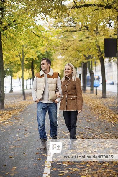Volle Länge des jungen Paares  das im Herbst auf der Straße läuft.