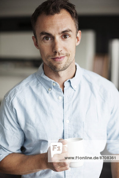 Portrait of confident businessman holding coffee mug in office