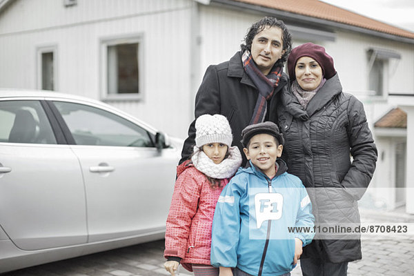 Porträt einer glücklichen muslimischen Familie in warmer Kleidung vor dem Haus stehend