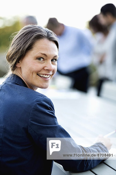 Porträt einer glücklichen Geschäftsfrau auf der Terrasse mit Kollegen im Hintergrund