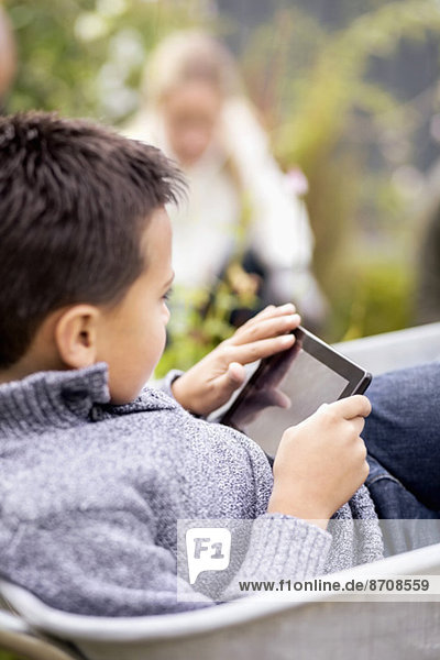 Junge mit digitalem Tablett im Schubkarren sitzend mit Mutter im Hintergrund