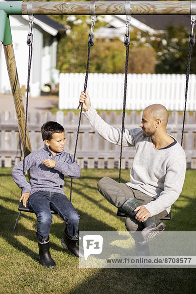 Father and son sitting on swings in garden
