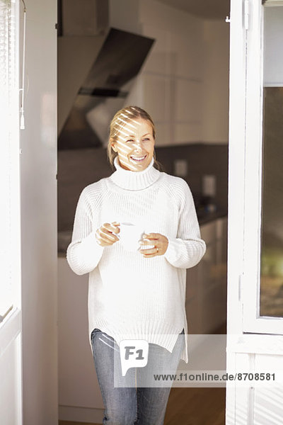 Glückliche reife Frau mit Kaffeetasse beim Verlassen des Hauses