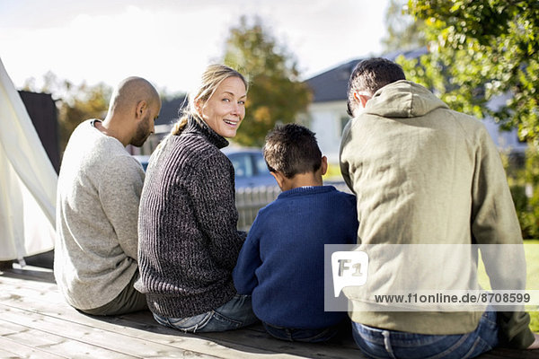 Rear view portrait of smiling woman sitting with family at yard