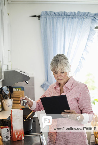 Seniorin beim Kochen  während sie sich das Rezept auf einem digitalen Tablett ansieht.