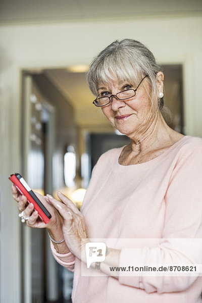 Porträt einer lächelnden Seniorin mit dem Handy zu Hause
